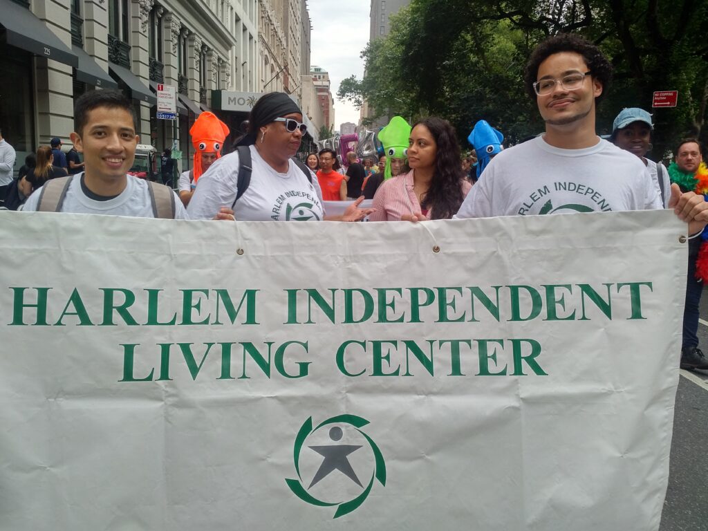 Two advocates march in a walk, holding a Harlem Independent Living Center sign high