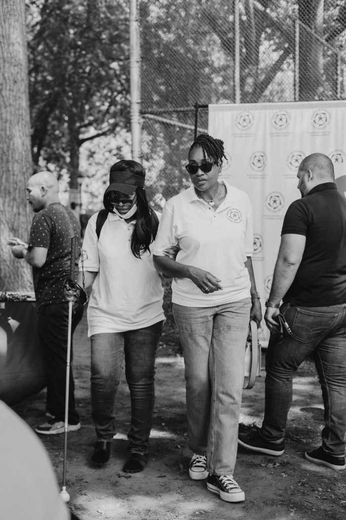 A picture of Yonette Lewis (Director of Operations) walking with Yasmin Campbell (Systems Advocate). Yasmin is walking with a cane and Yonette is guiding her.