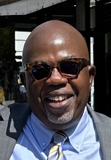 Portrait of Calvin. Calvin is wearing a grey suit ad blue shirt. Calvin is also wearig sun glasses
